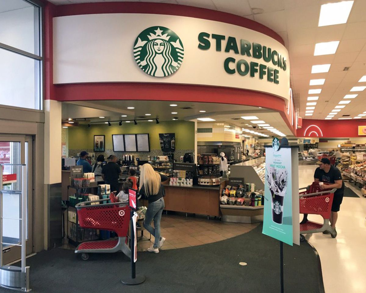 A Starbucks Coffee inside a Target store, entrance doors on the left, produce section on the background right, people with carts waiting around