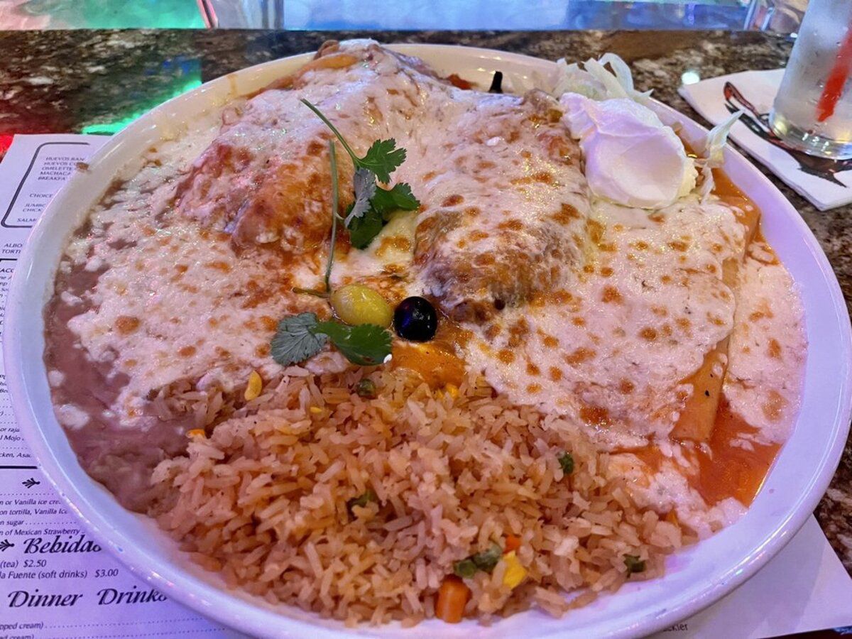 Chiles Rellenos and a Cheese Enchilada with sides on a white plate with a glass of water, El Compadre, Los Angeles, on a menu on a granite table at the restaurant, slight purple lighting