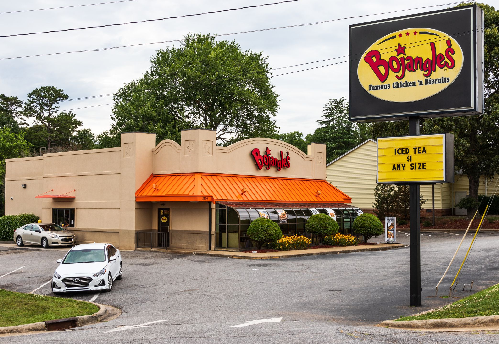 Exterior of Bojangles fast food restaurant, Hickory, North Carolina, surrounded by parking, with a car in drive-thru, sign is in the foreground, with trees and a blue sky with clouds in the background