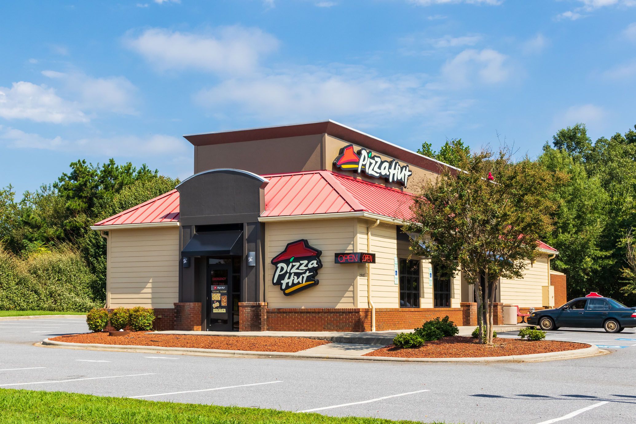 Exterior of Pizza Hut restaurant in Hickory, North Carolina surrounded by an empty parking lot with trees against a blue sky in the background