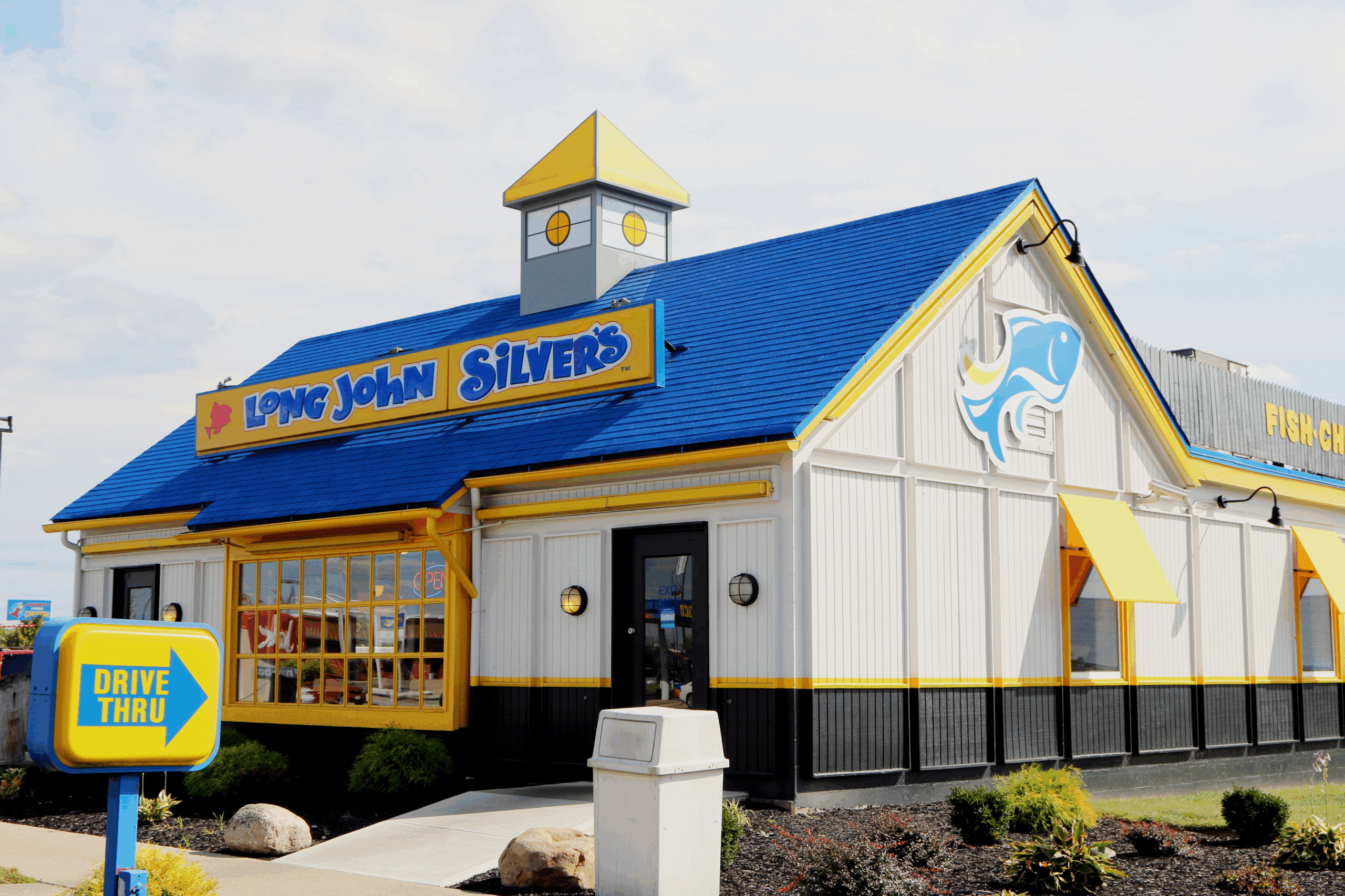 Front exterior of Long John Silver's seafood restaurant, Lexington, Kentucky, surrounded by garden, and side-view, drive-thru sign, against a white cloud day