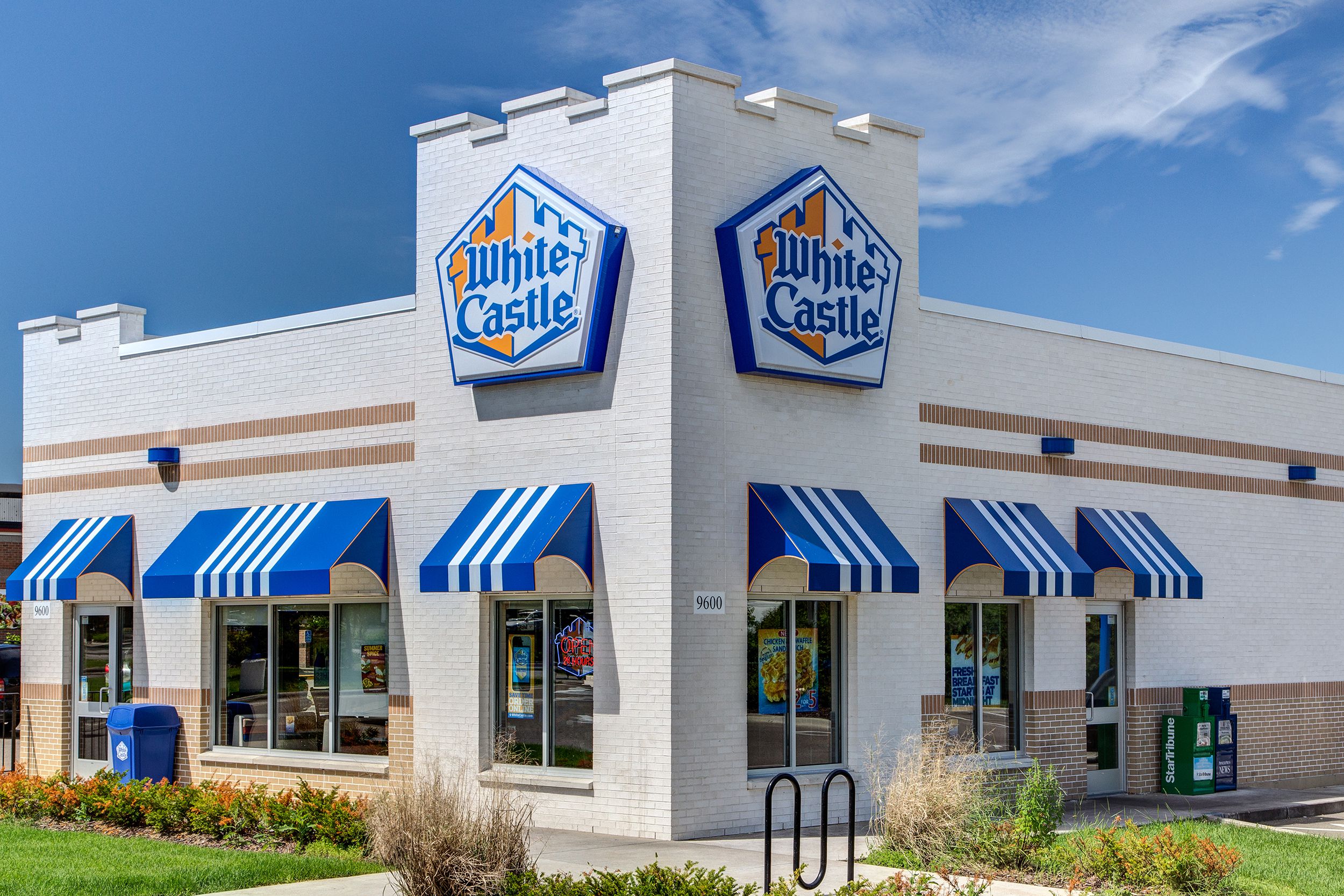 Front exterior of White Castle fast food restaurant, Bloomington, Minnesota, windows, front doors, and side doors, bright white building, surrounded by a garden, against a blue sky on a sunny day