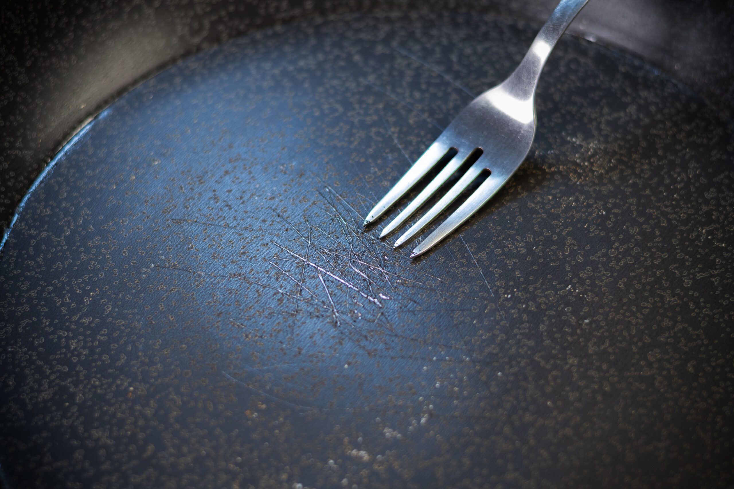 Scratched nonstick pan with a fork pointing at the scratches