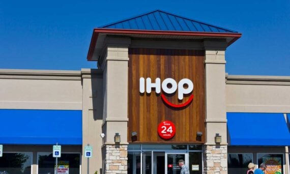 The front of an IHOP restaurant with a large IHOP logo, blue awnings, and a sign indicating it is open 24 hours; handicap parking signs are visible in front.