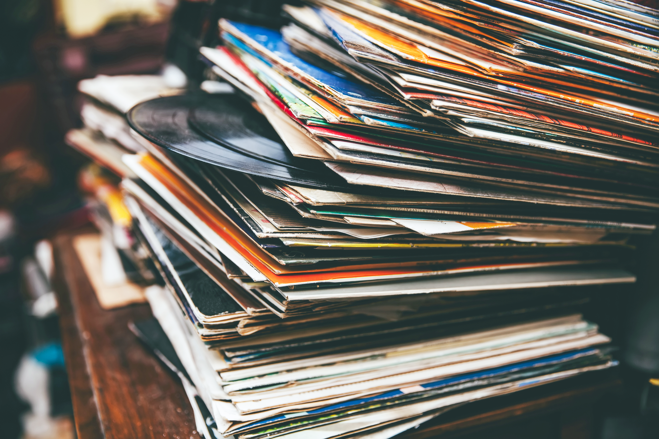 Large stack of vinyl records on a wooden table with a blurred background, image has vintage coloring