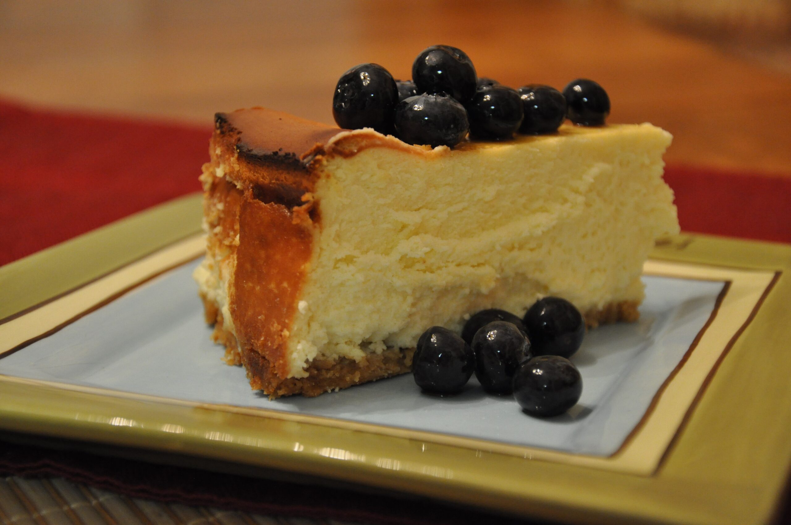 Slice of New York Cheesecake with fresh blueberries on a white and gold square plate