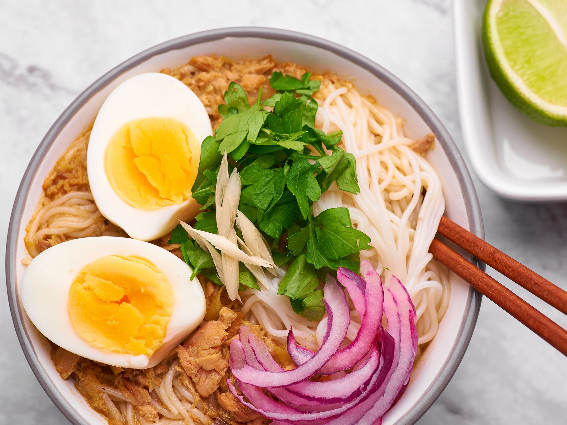 Mohinga at white marble background. Mohinga is a burmese cuisine fish soup with catfish, rice noodles, chicken eggs and lime.