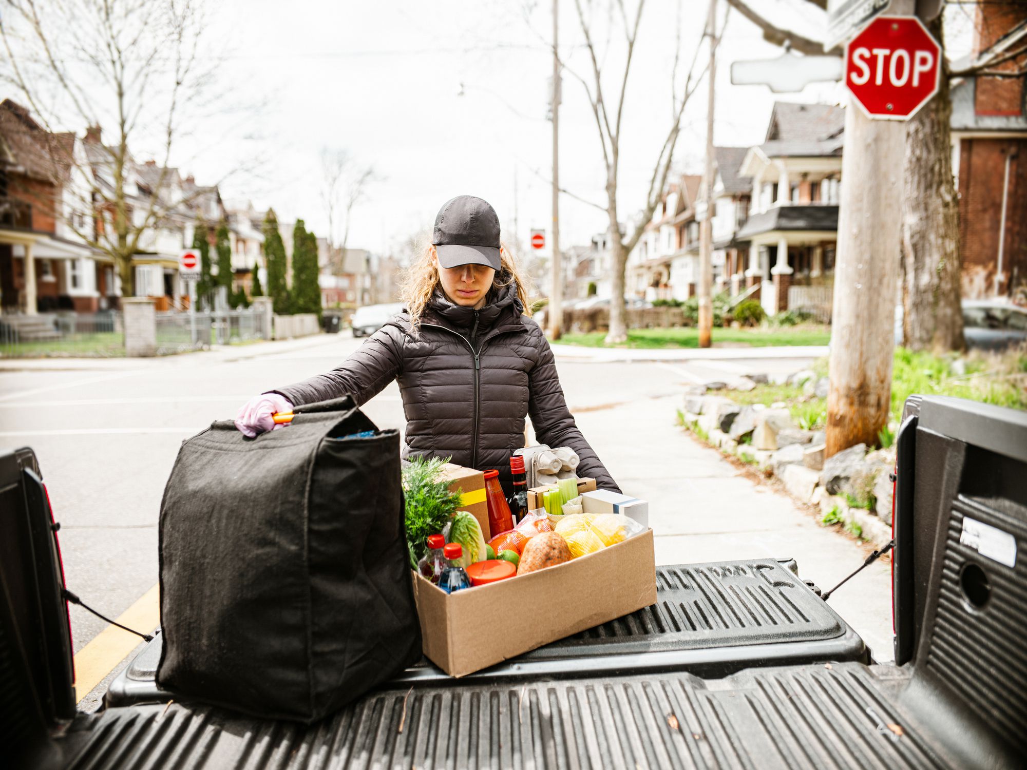 Young women delivers fresh food during pandemic lockdown. She is offloading box of fresh produce from the bed of the pick up truck. Urban setting of a North American city.