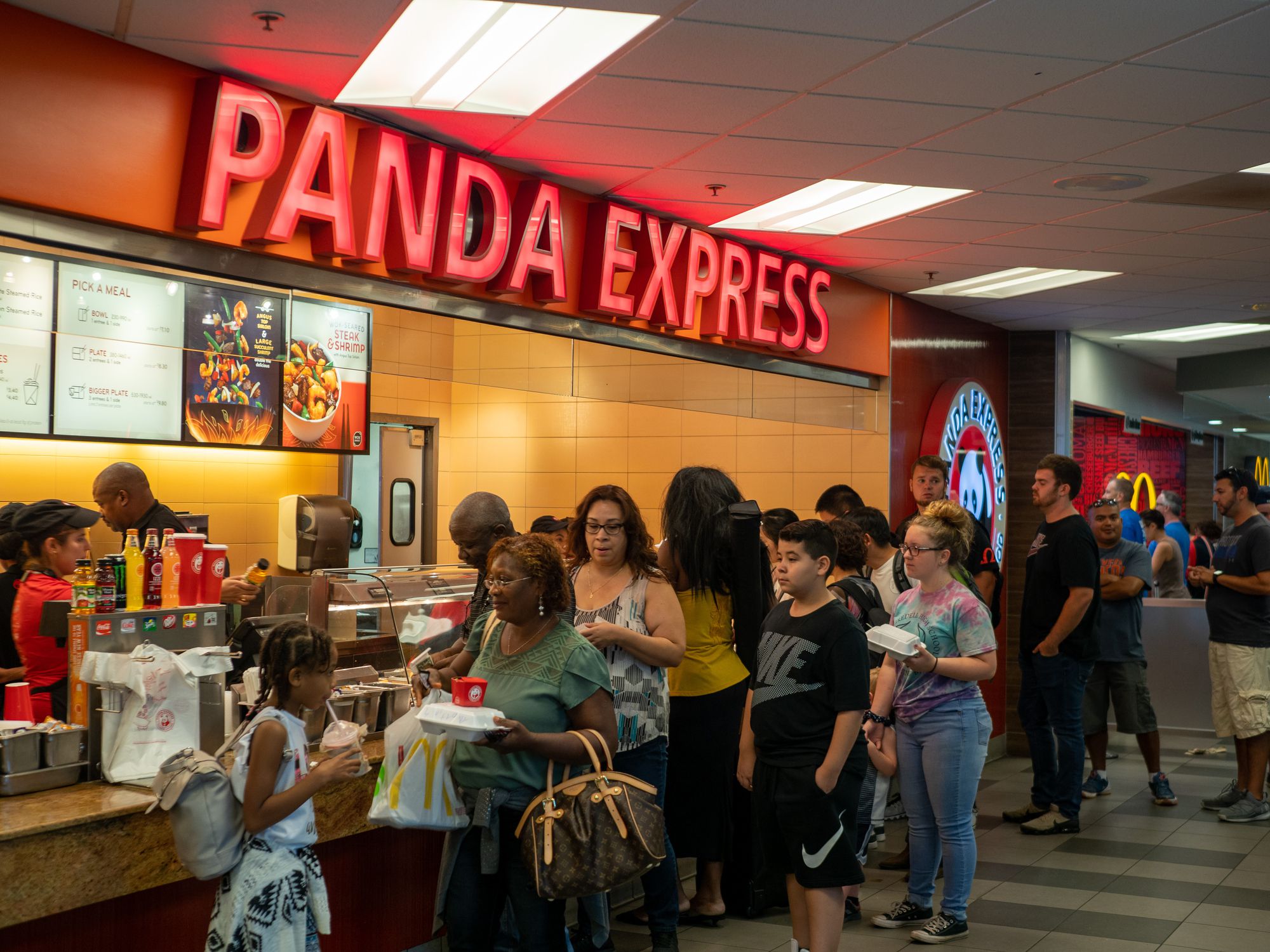 Several people wait in line at an Panda Express fast food take out restaurant in a food court, Denver, with a McDonalds in the background