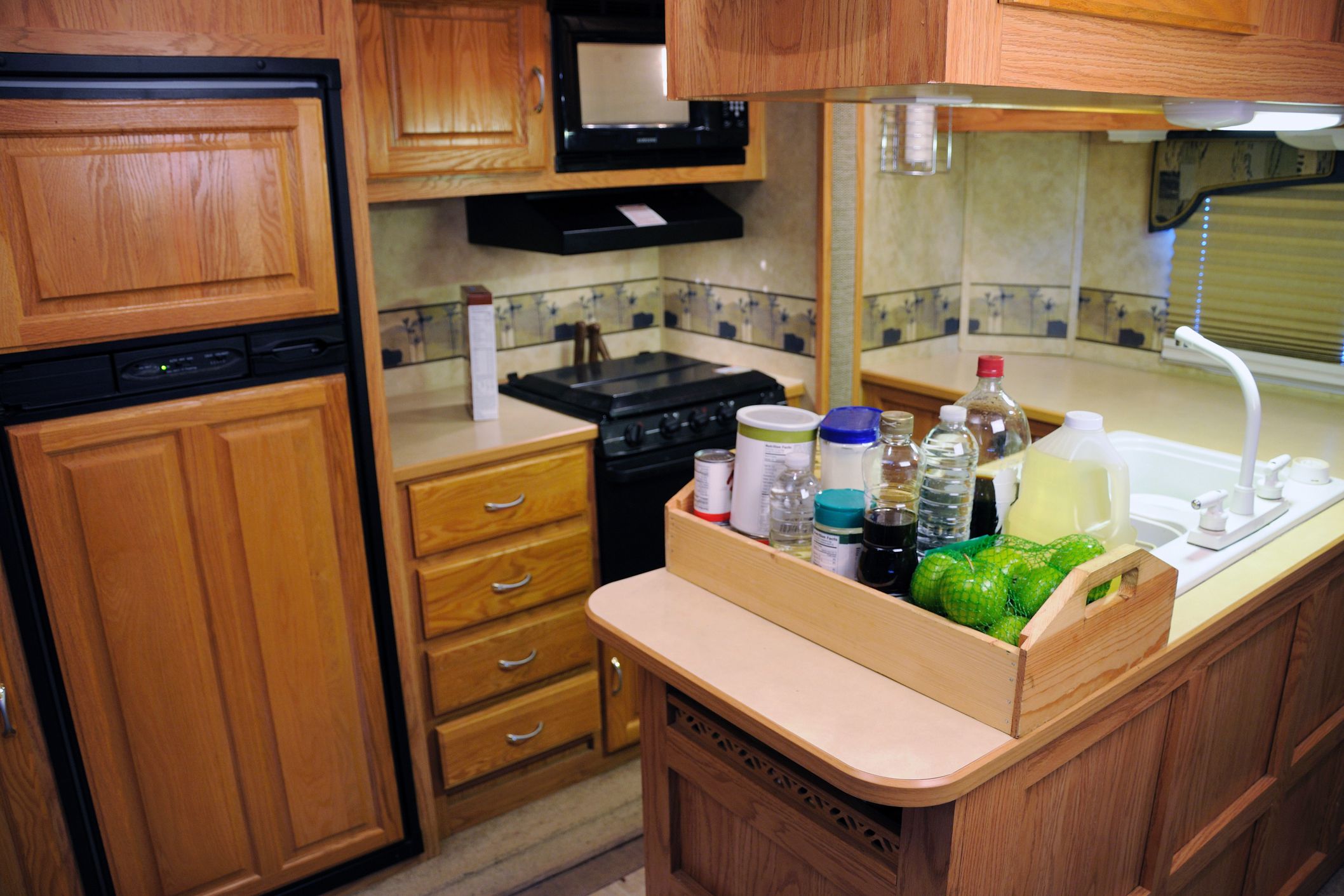 Spacious kitchen in an RV, food on countertop of the island with a white sink, wooden cabinets