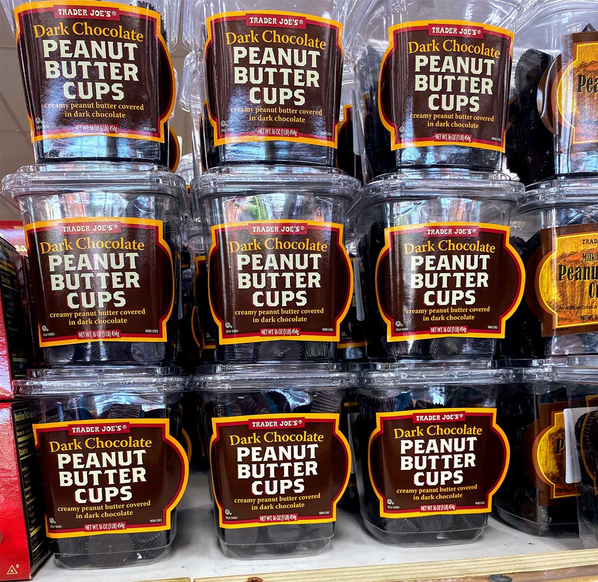 Stacks of Trader Joe’s Dark Chocolate Peanut Butter Cups in clear plastic containers are displayed on a store shelf, their bold orange and black labels highlighting one of the most popular Trader Joe's desserts.