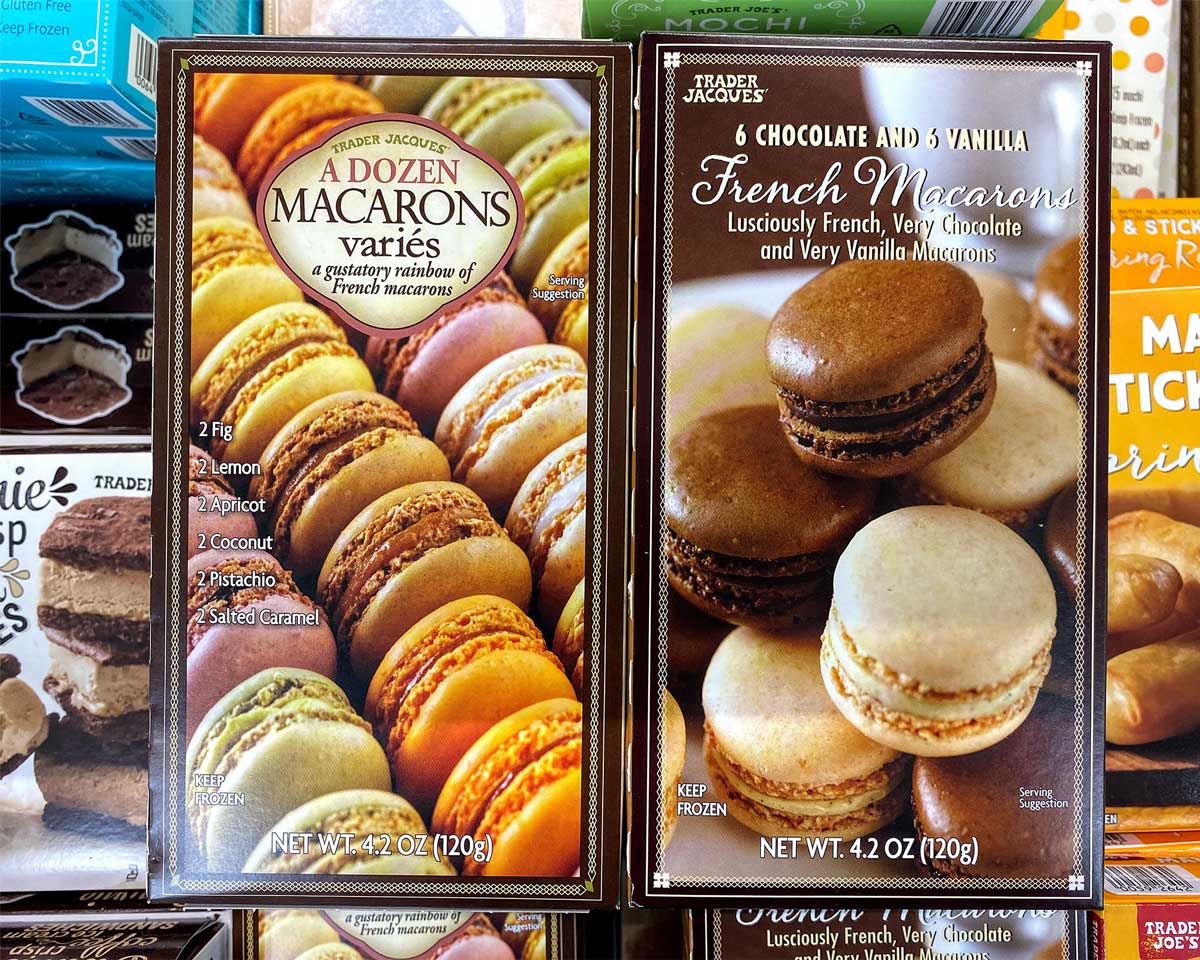 Two boxes of Trader Joe’s desserts are displayed side by side. The left box holds twelve assorted macarons in vibrant colors and flavors; the right box features six chocolate and six vanilla macarons.