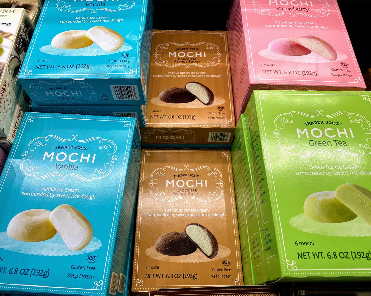 Boxes of Trader Joe’s Mochi ice cream—one of the popular Trader Joe's desserts—in vanilla, chocolate, strawberry, and green tea flavors are stacked side by side. Each box features mochi images and contains six delicious treats.
