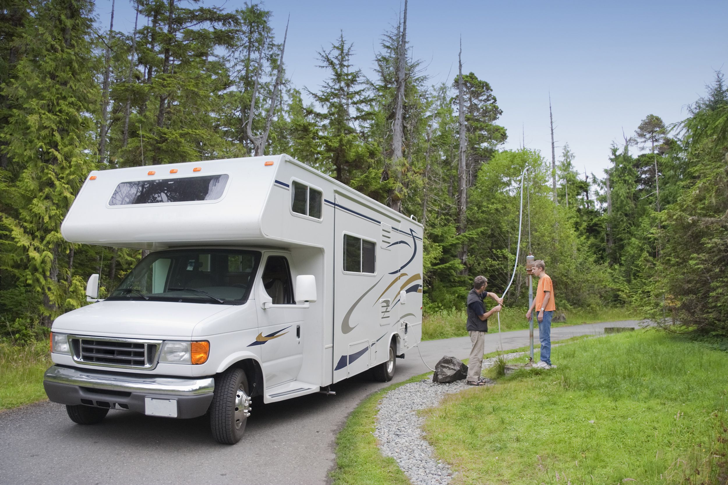 Two people at a dumping station with an RV on the left, people on the right, surrounded by forest, blue sky in the background