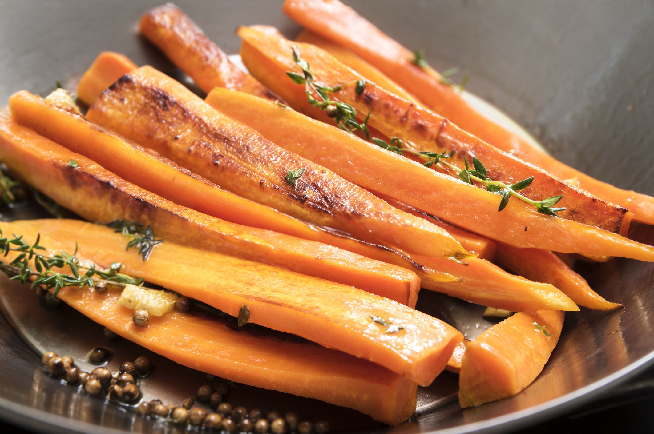 roasted carrots with thyme, coriander seed and honey in a wok pan, recipe for root vegetables, selected focus, narrow depth of field