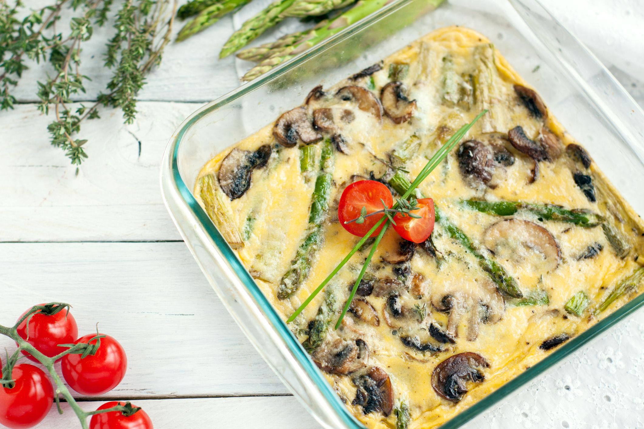 Delicious asparagus and mushroom frittata served in glass baking dish garnished with cherry tomatoes and greens
