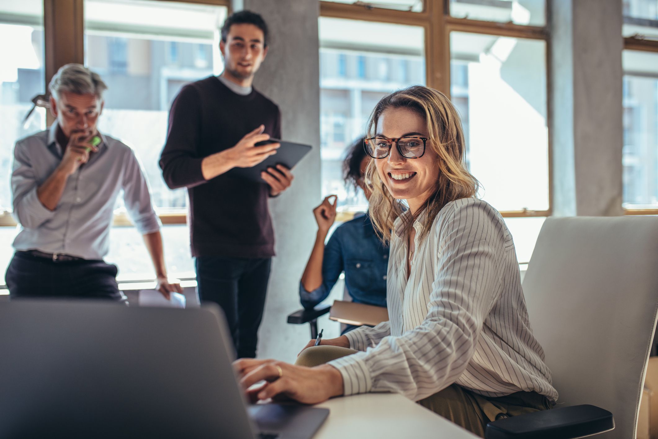 Female entrepreneur working on laptop and explaining strategy to attract followers to online web store while having meeting with colleagues in office.