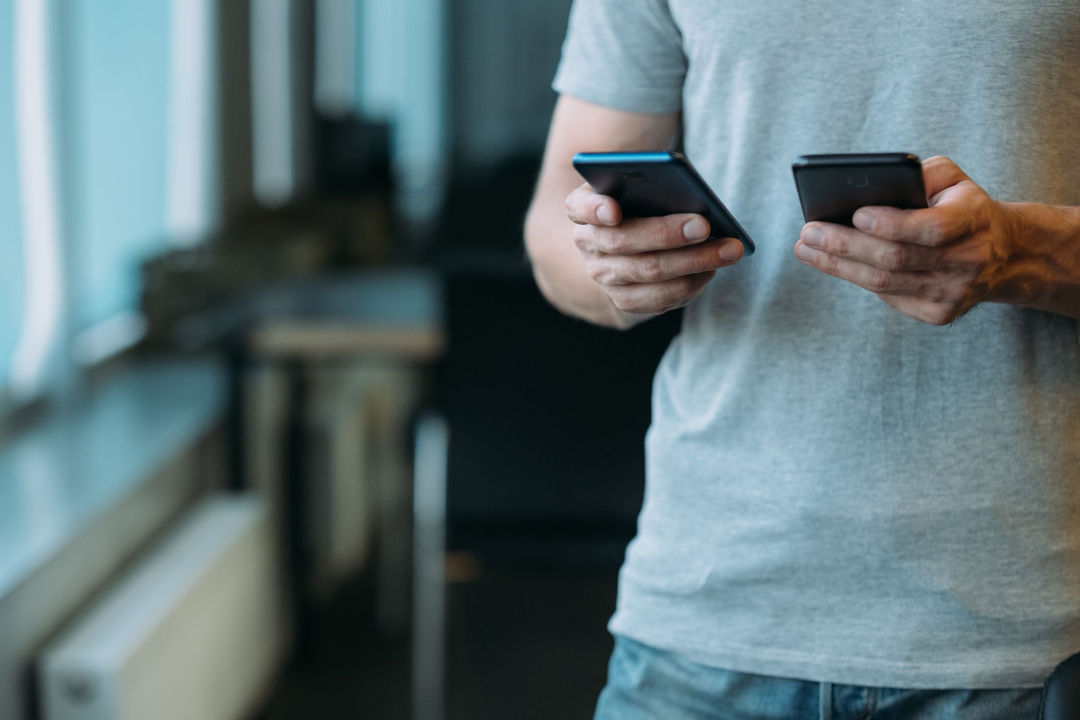 Online business communication. Cropped shot of man using two smartphones. Blur office background.