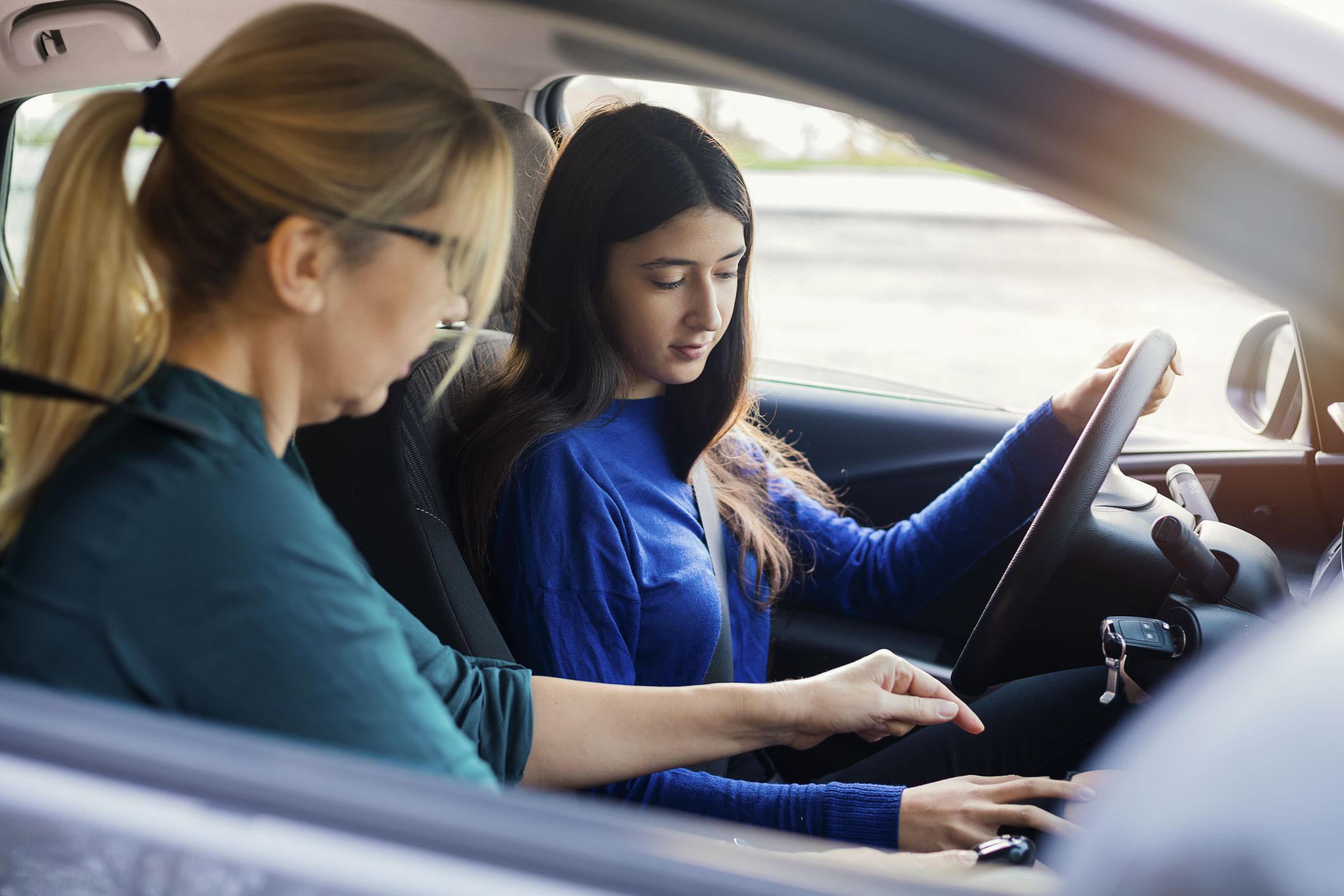 A teenage girl sitting behind the steering wheel of a car and listening to her mothers instructions as she drives.