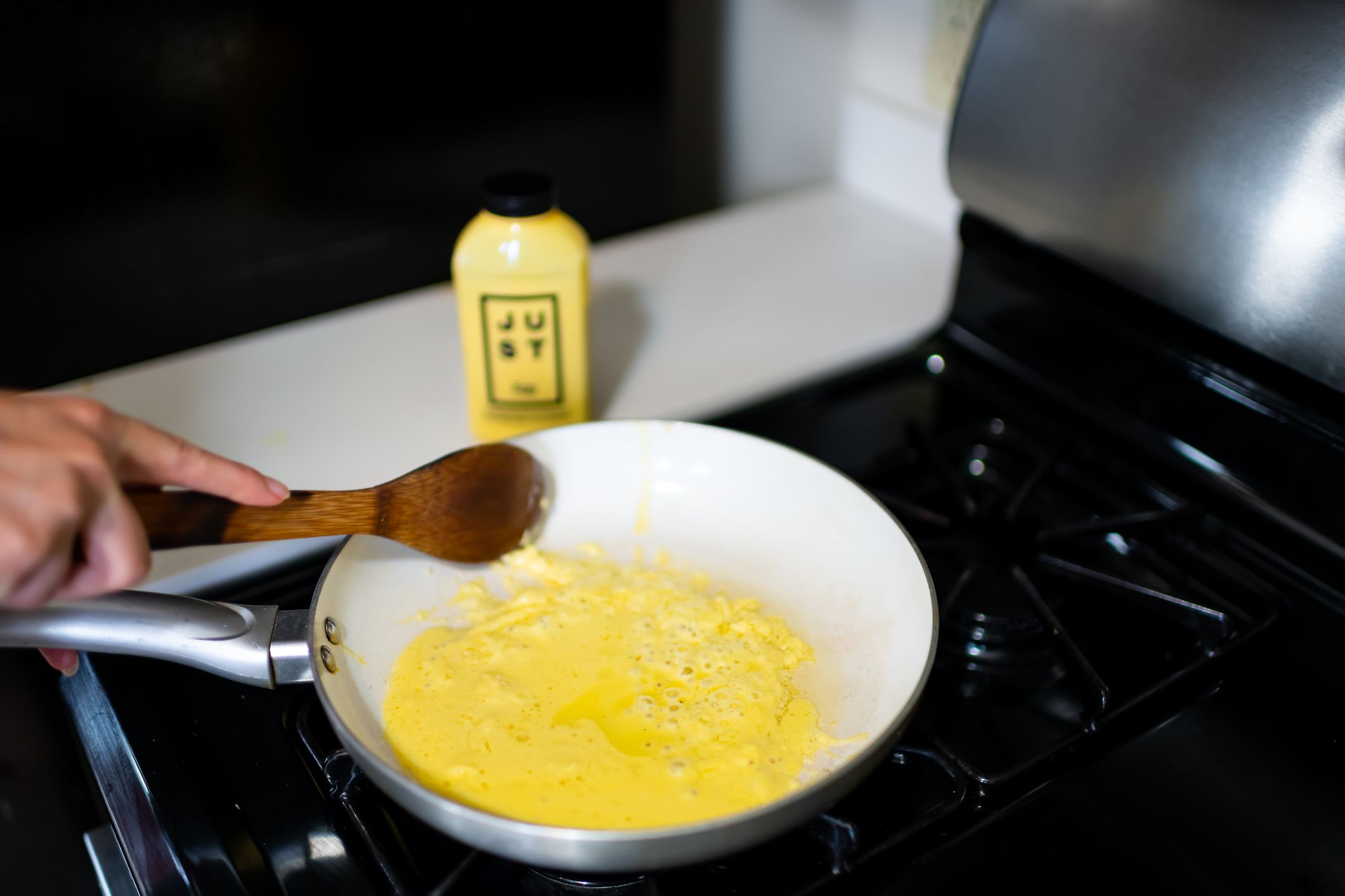 Aspen, USA - September 20, 2019: Woman cooking Just Egg substitute for scrambled omelette with wooden spatula in ceramic frying pan