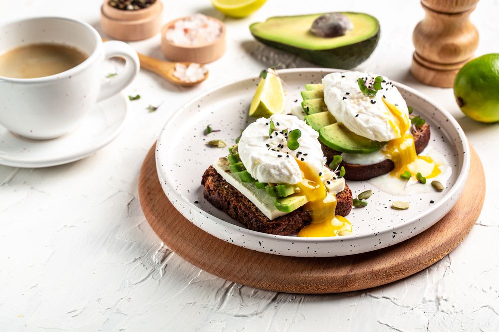 Sandwich with avocado and Poached Egg. Wholemeal Bread Toast sliced avocado and egg with cup of coffee for healthy breakfast or snack, copy space