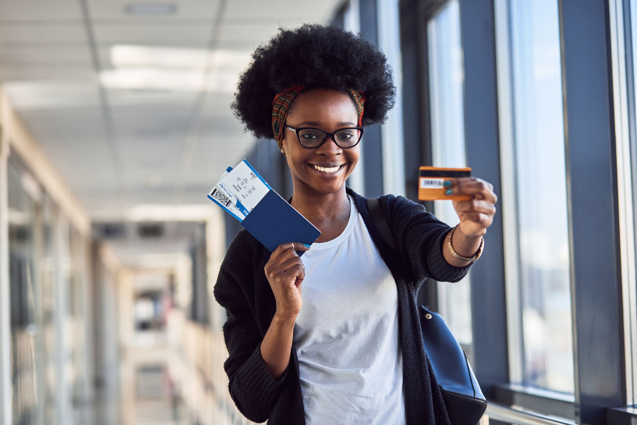 Young african american female passanger in casual clothes is in airport holding tickets and credit card.