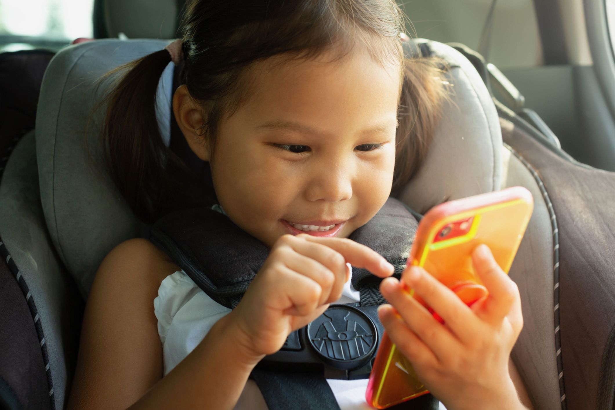 A young kid using a smartphone sitting in the car seat during a trip.