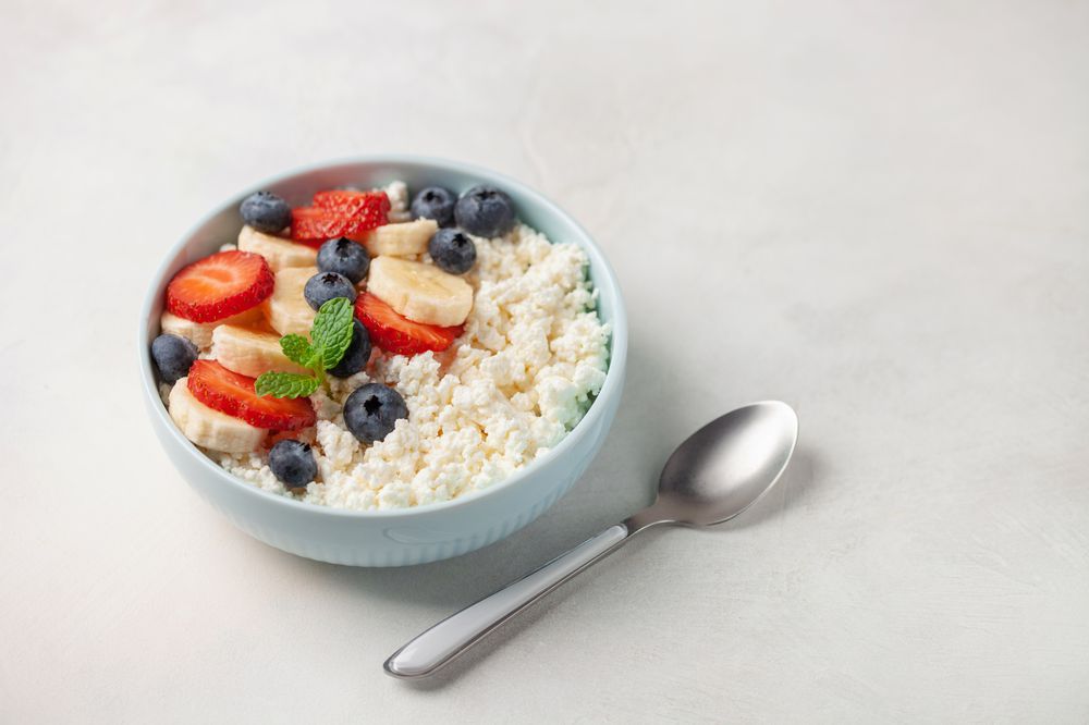 Healthy breakfast - cottage cheese with banana and berries in a bowl on the table.