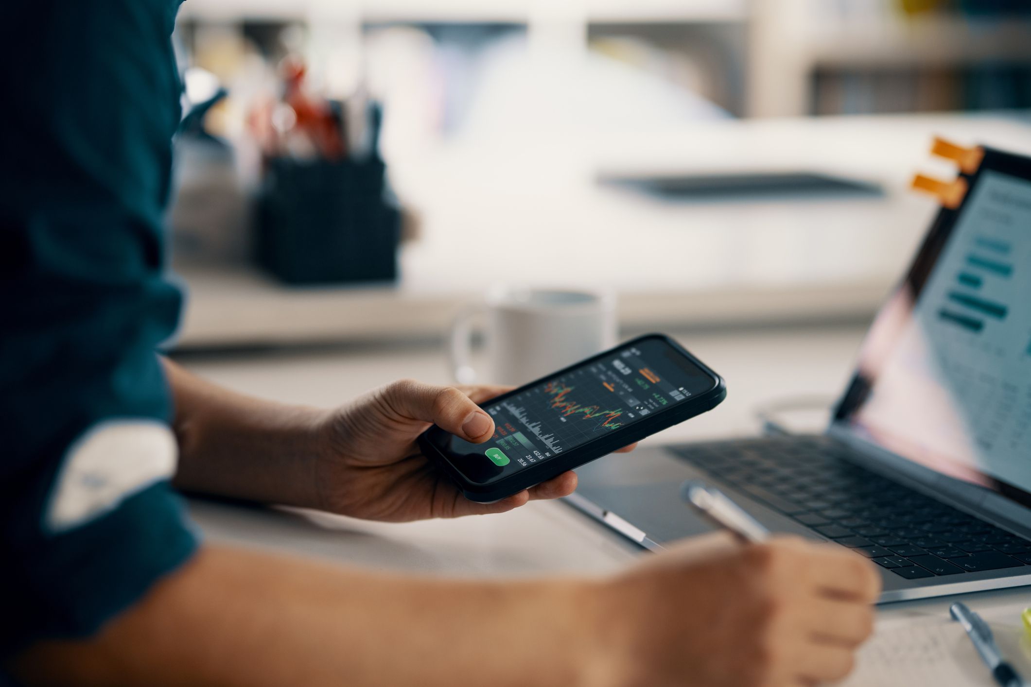 Mid adult man checking financial information on a smart phone while doing his bookkeeping in his home office in Japan. Depicts TradingView financial market chart.