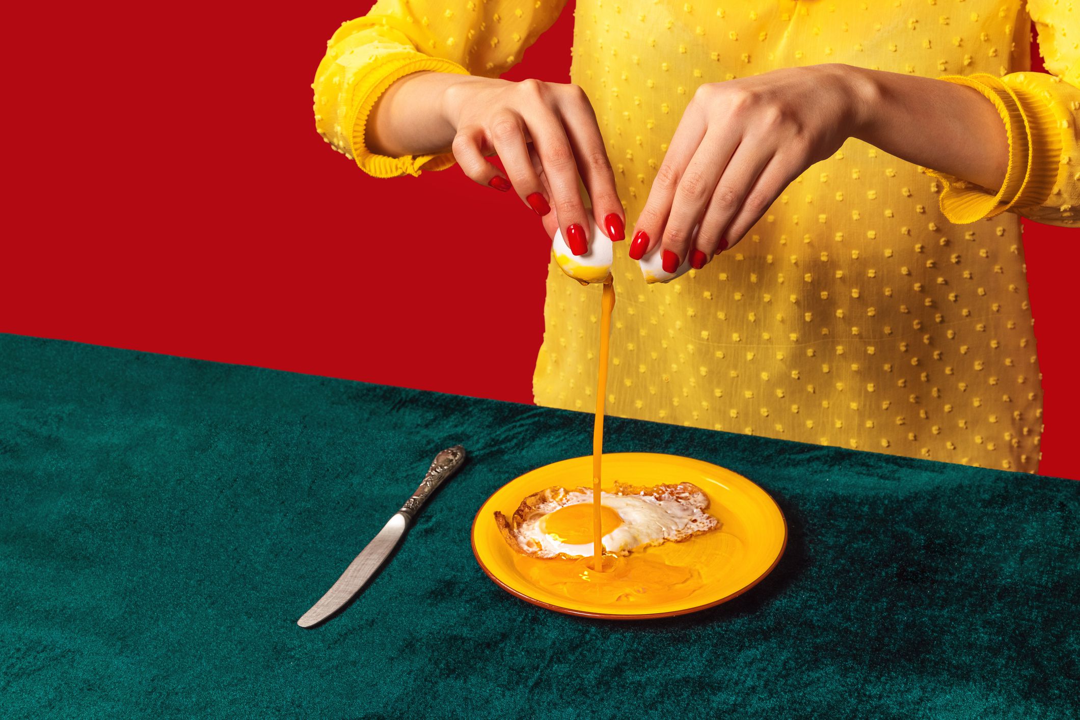 Woman cooking fried eggs on plate isolated on green and red background. Vintage, retro style interior. Food pop art photography. Complementary colors, red, green and yellow. Copy space for ad, text