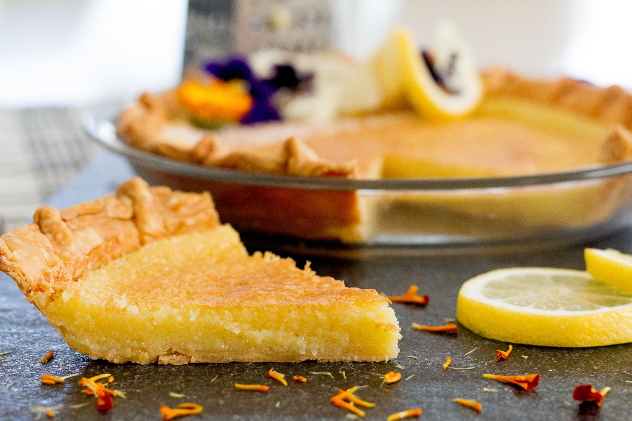Freshly made lemon coconut pie, made with lemon extract, sugar, eggs, shredded coconut, shredded squash, and flour, baked in a pie shell and garnished with edible flowers and shredded coconut.