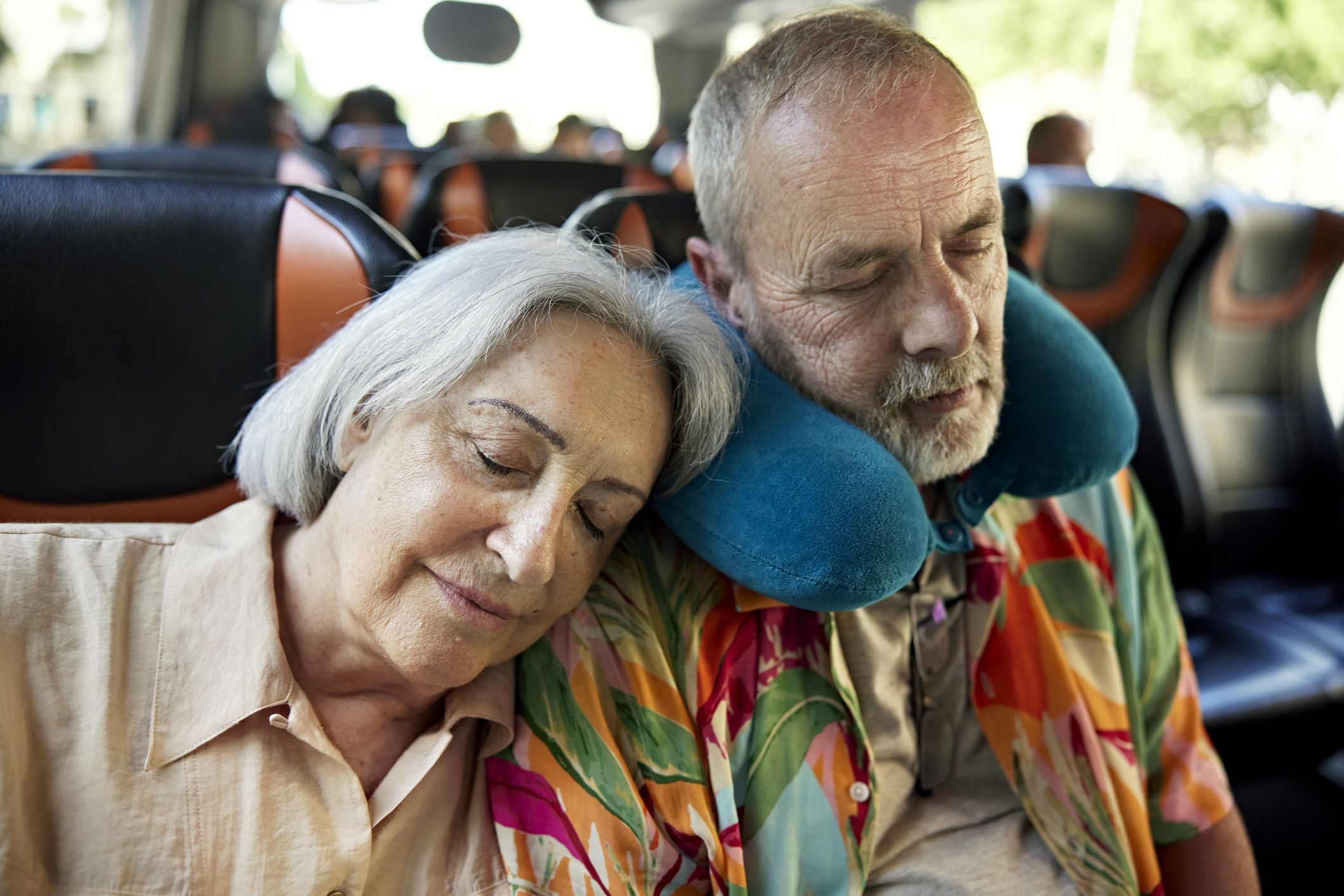 Head and shoulders view of vacationers in 60s and 70s sitting side by side with eyes closed as they travel to their destination.