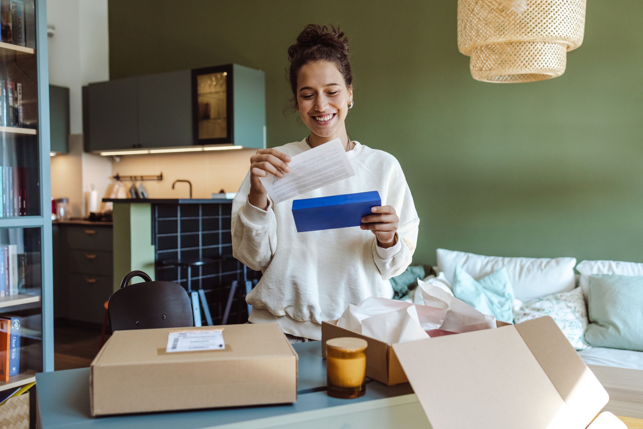 Beautiful young woman opening a cardboard box in the living room and reading thank you letter