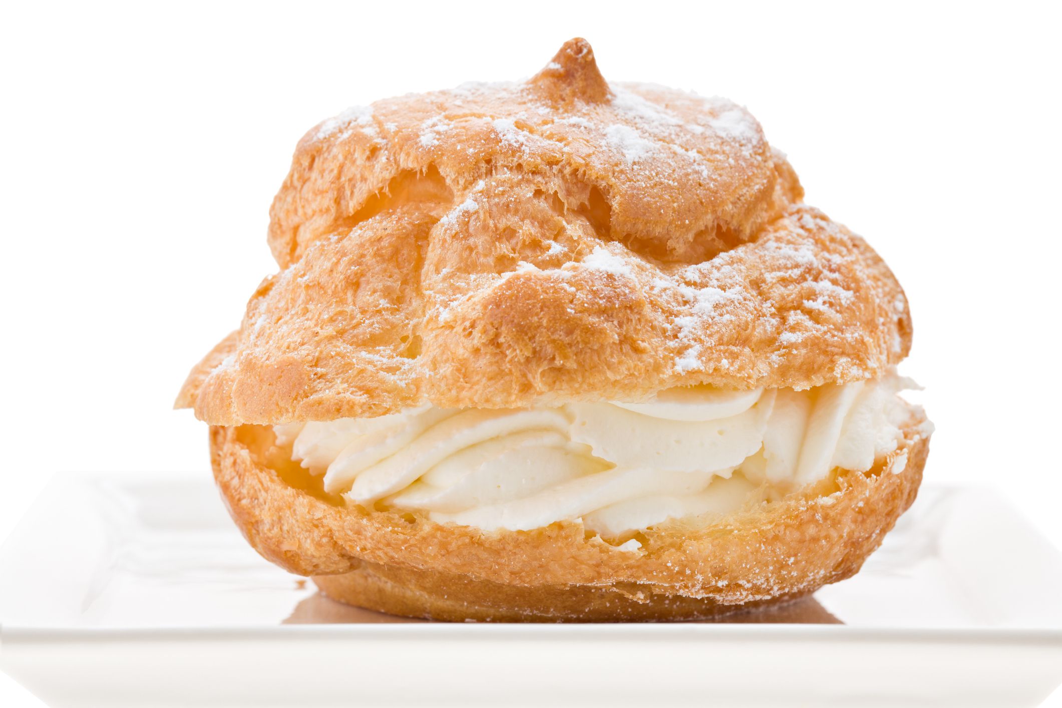 An extreme close up of a cream puff on a square white plate. Isolated on white.