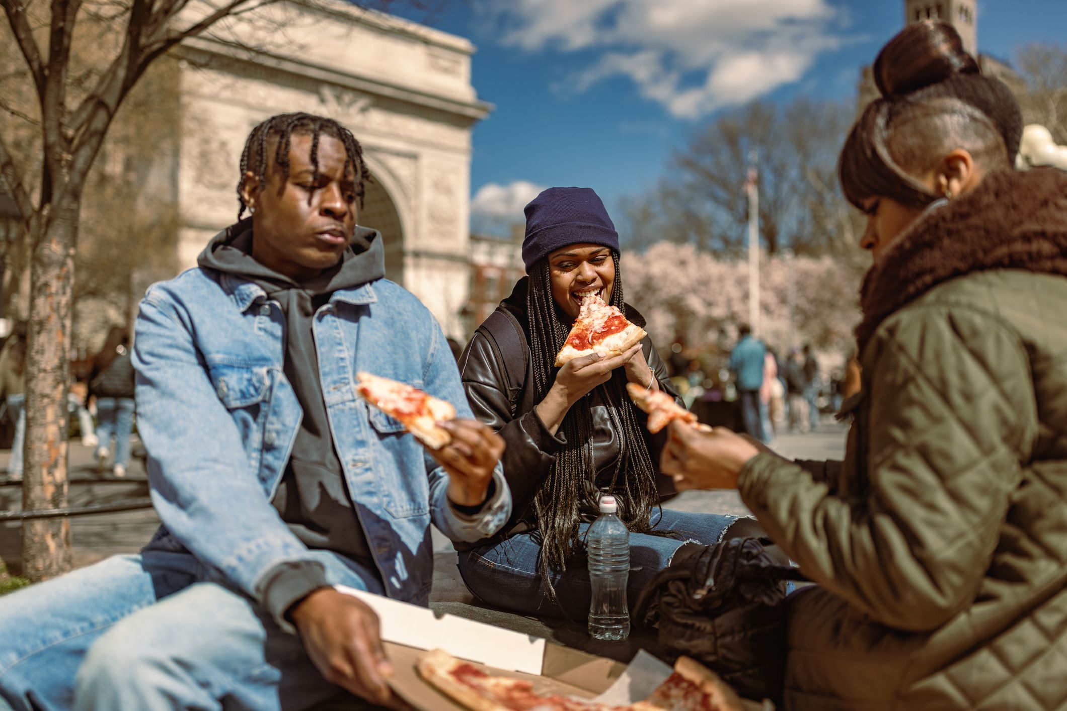 Three friends enjoying pizza in the park on a sunny day. Washington Square Park