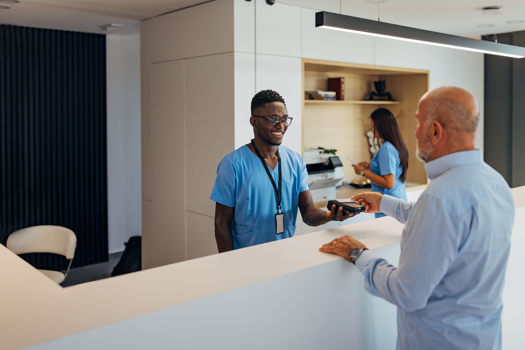 Senior patient making payment using credit card contactless with a credit card reader machine in modern clinic
