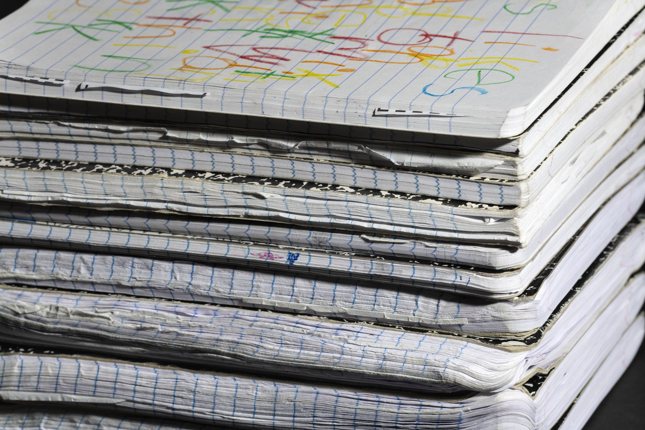 A stack of well-used notebooks with worn edges and colorful scribbles on the top cover, showcasing creativity and everyday use. Ideal for education or writing-related themes.
