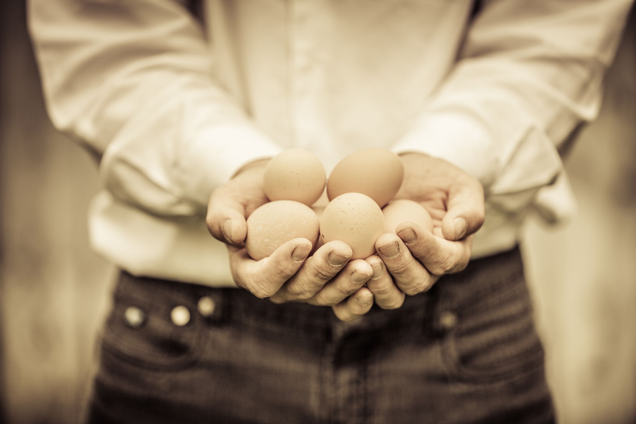 Closeup of Farmer Holding Eggs in front of a Farm