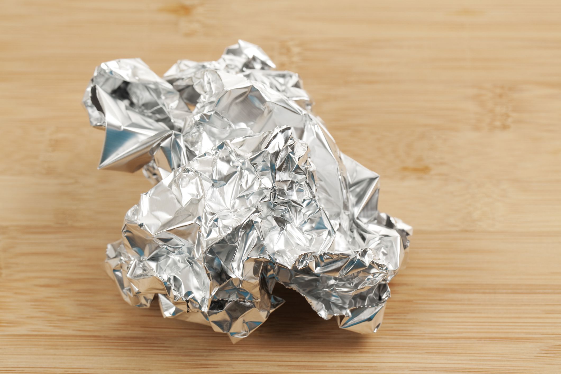 Aluminum Foil Ball. Crumpled aluminum foil ball on a wooden surface. Shot in studio with Canon 5D Mark II DSLR camera.