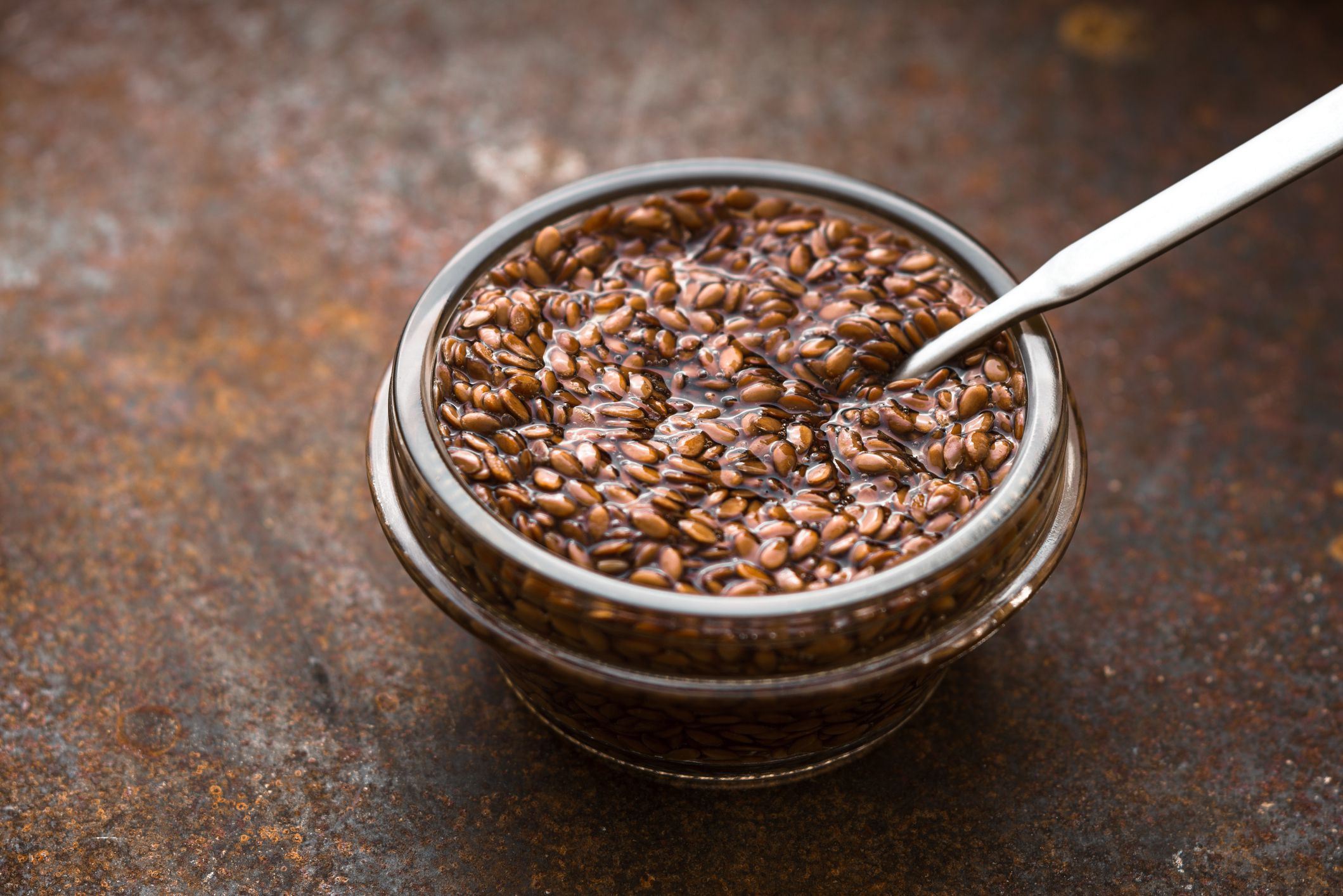 Glass bowl with flax seeds in the water on the old metal background horizontal