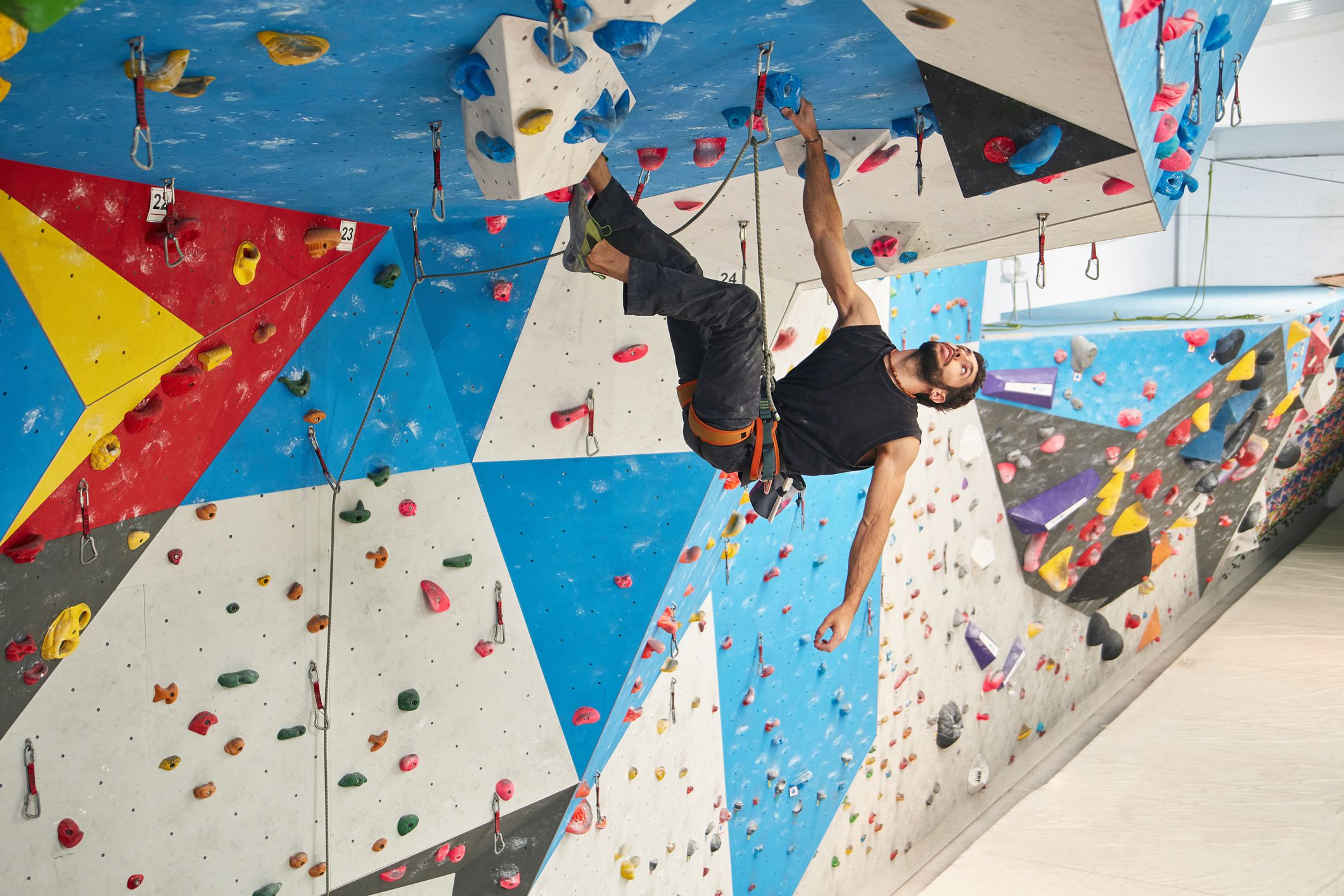 Full length of young man climbing wall in gym. Low angle view of male is exercising. He is in sports clothing.