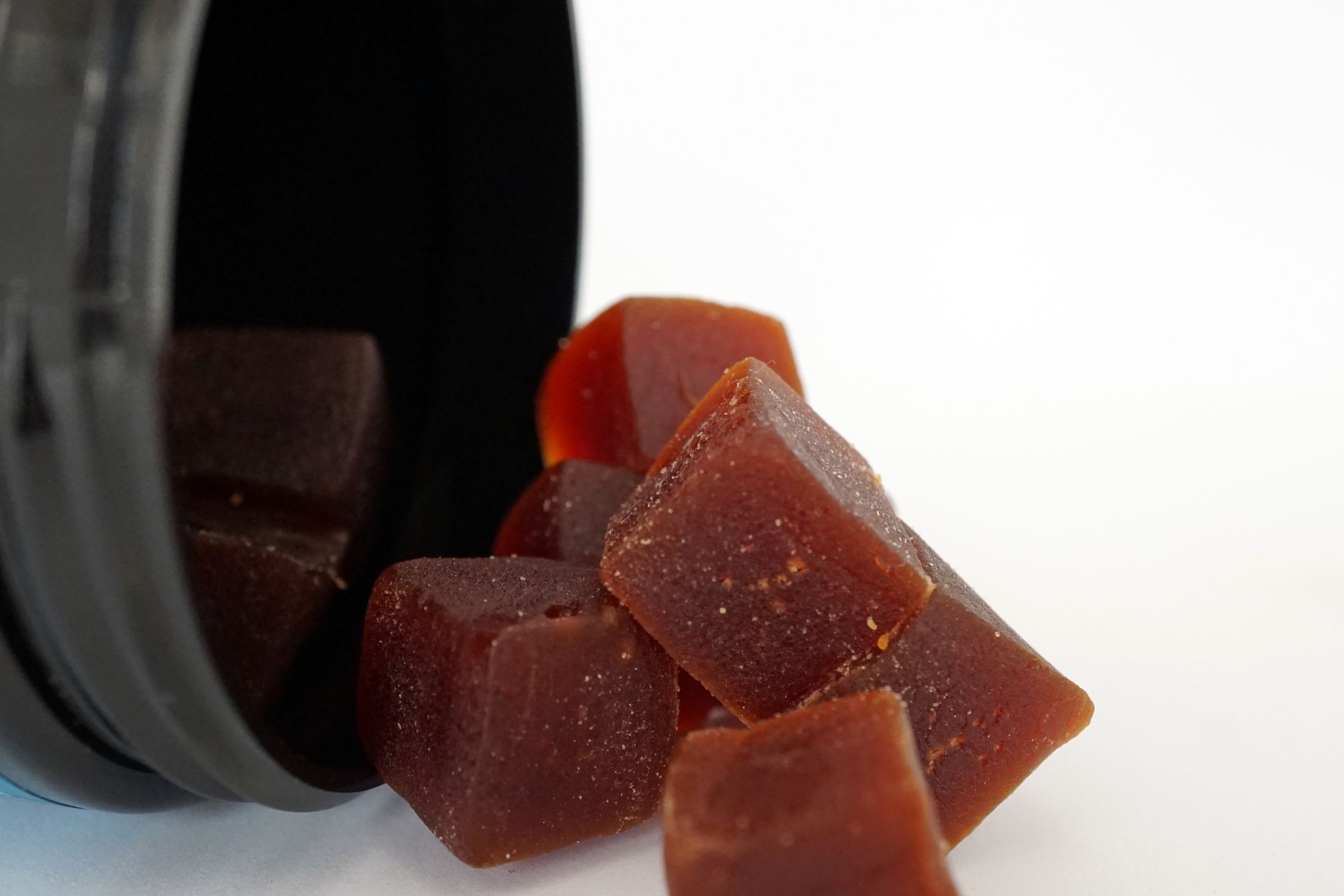 Closeup of square maroon CBD gummies out of black container against a white background