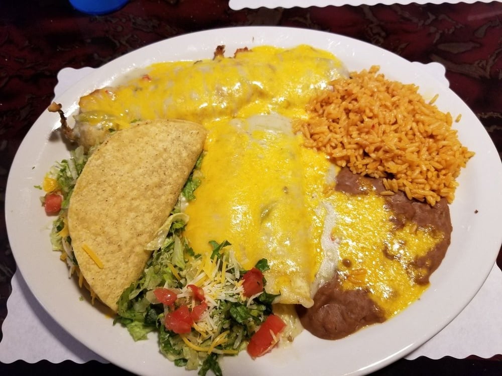 A plate of Mexican food with two cheese-covered enchiladas, a crunchy taco filled with lettuce, tomato, and cheese, a serving of refried beans, and a portion of Mexican rice.
