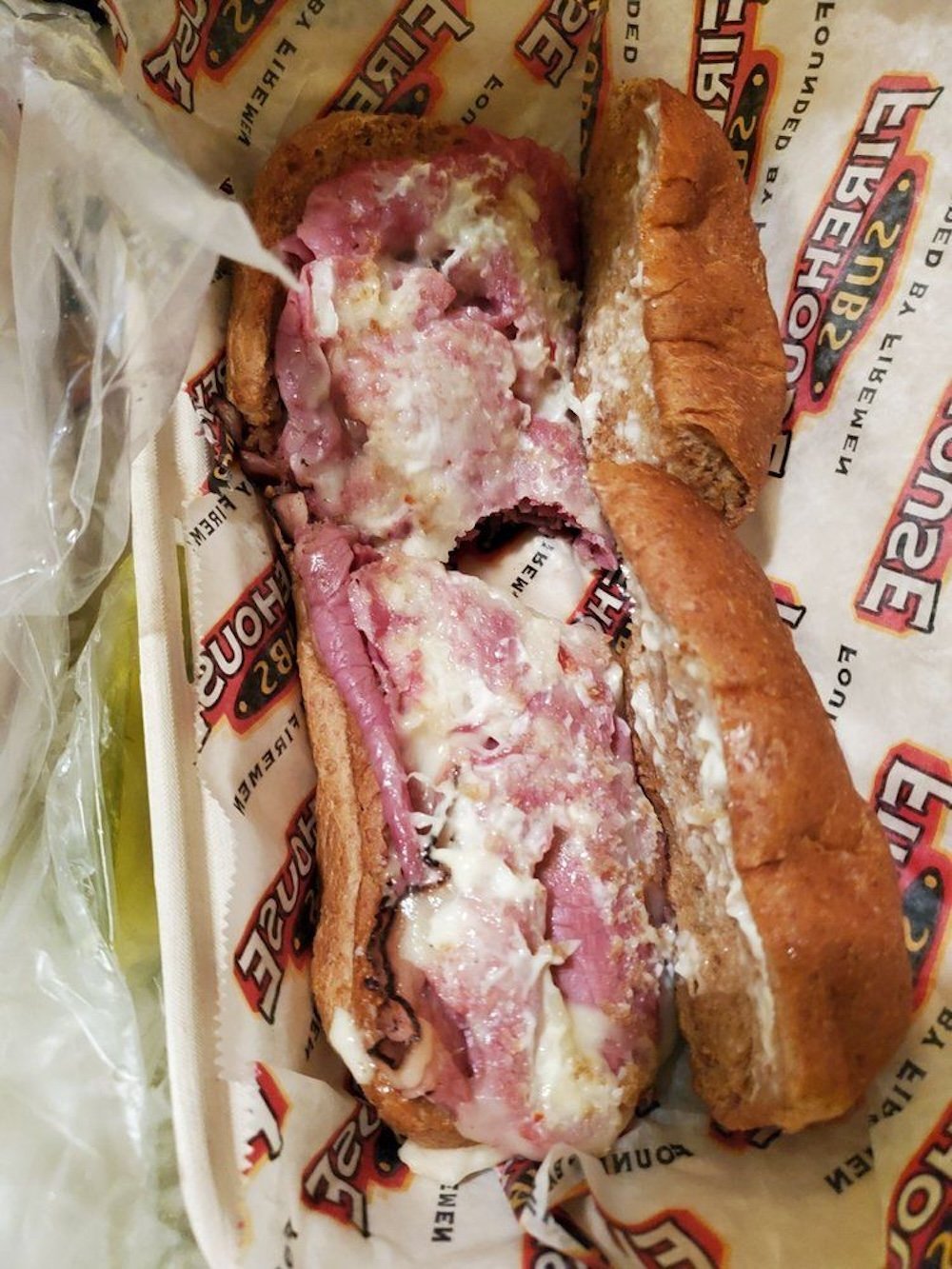A sub sandwich on brown bread filled with slices of roast beef and melted cheese, served on Firehouse Subs branded paper.