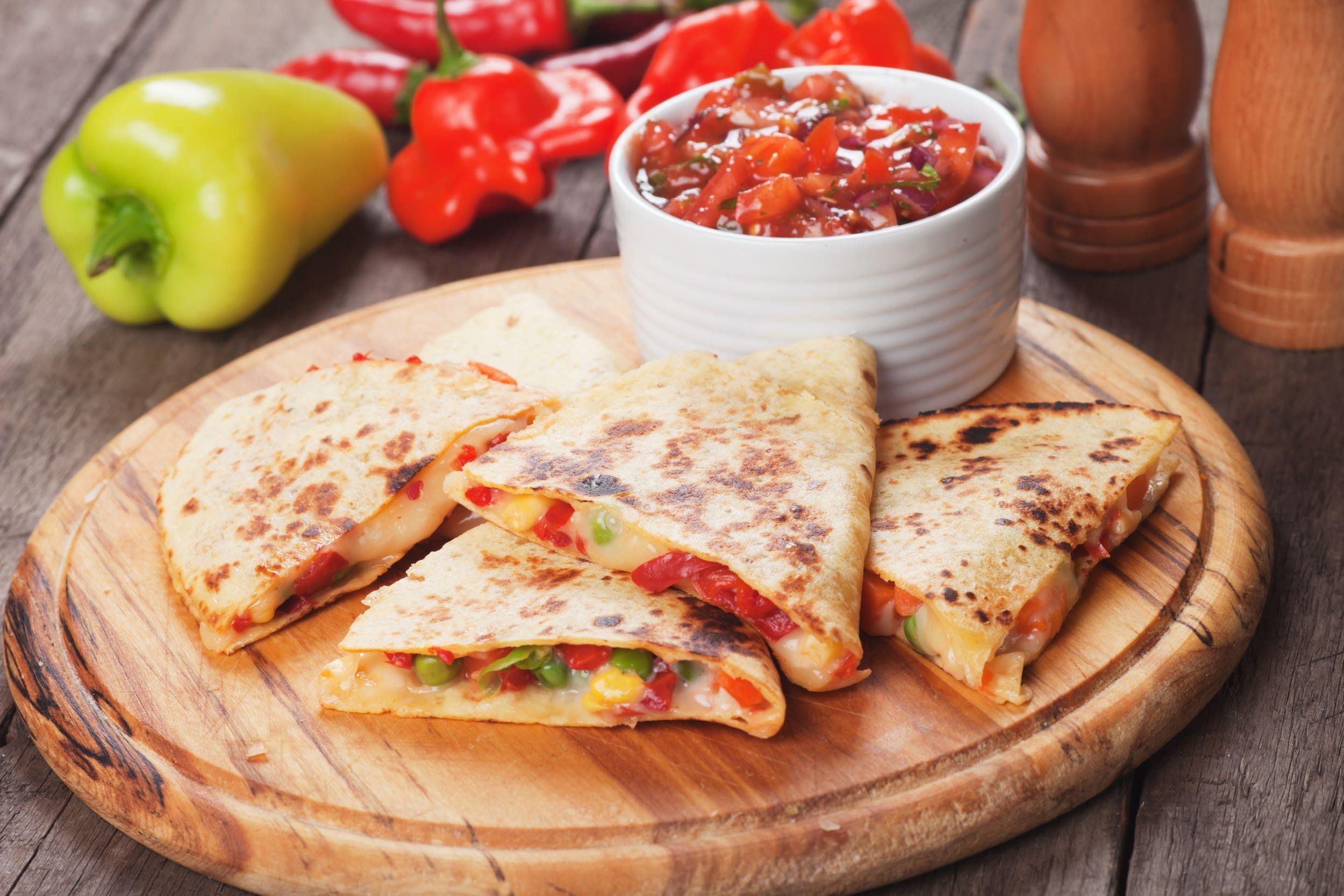 Quesadilla on a circular cutting board with a white cup of salsa