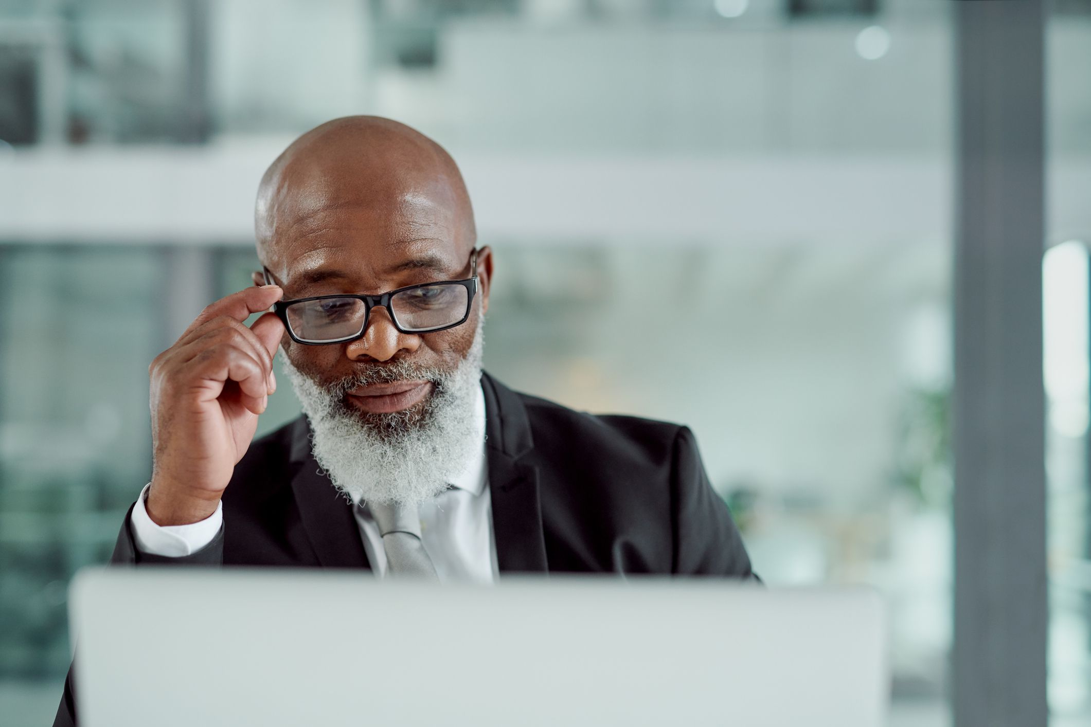 Senior business man concentrating in front of a computer in an office with a blurred background of large window and another building