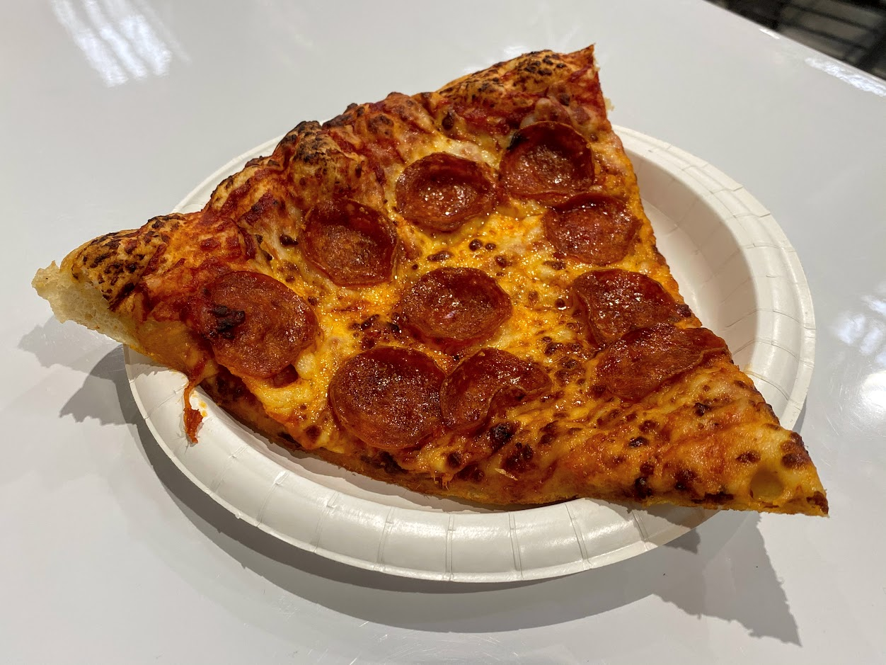 Slice of a pepperoni pizza on a white paper plate at the Costco food court, on a white table
