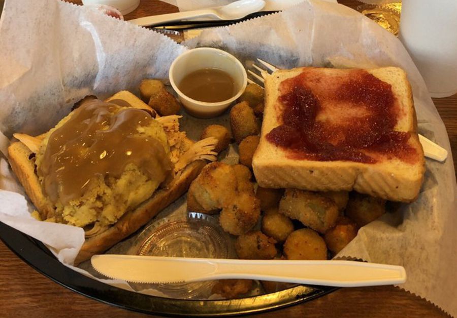 The Turkey Day Sandwich in a black basket, The Fried Turkey Sandwich Shop, Fayetteville, North Carolina, a person eating another sandwich across from it, on a wooden table