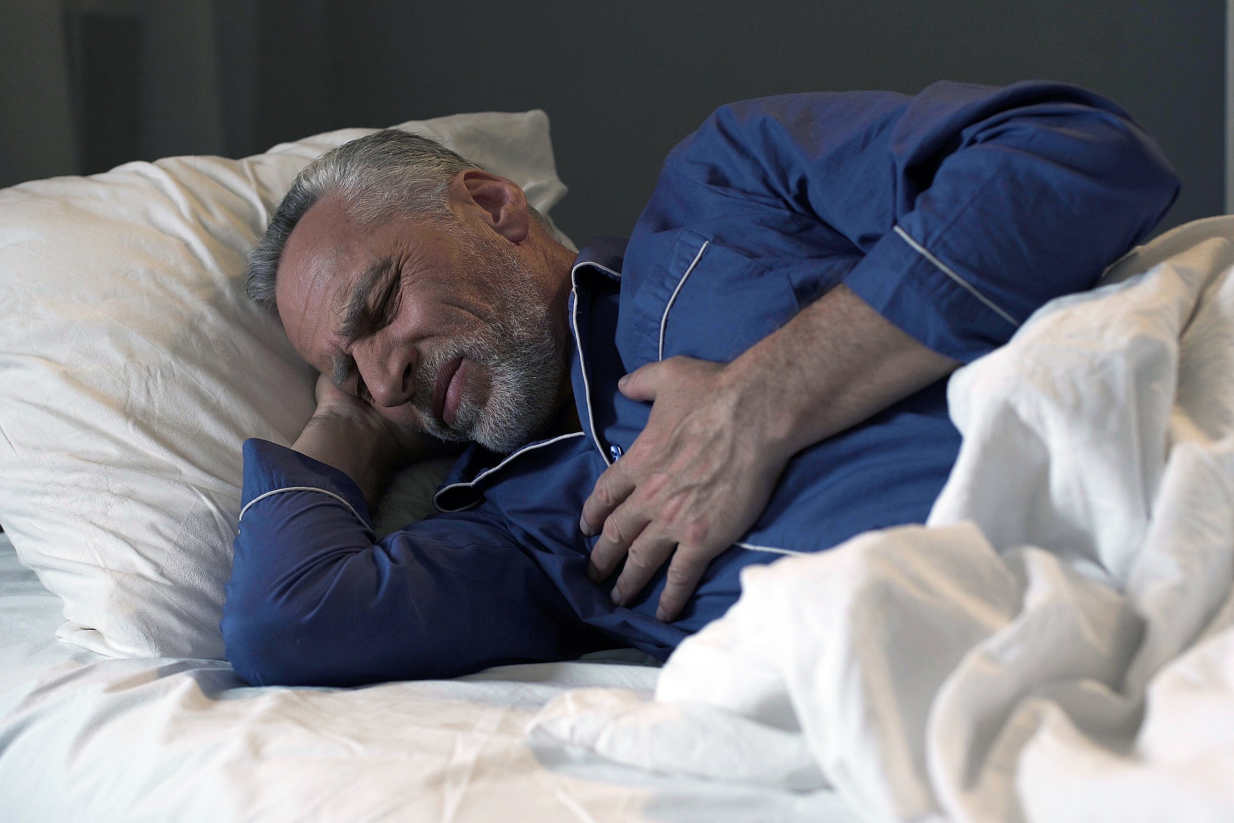 Older man experiencing chest pains in bed