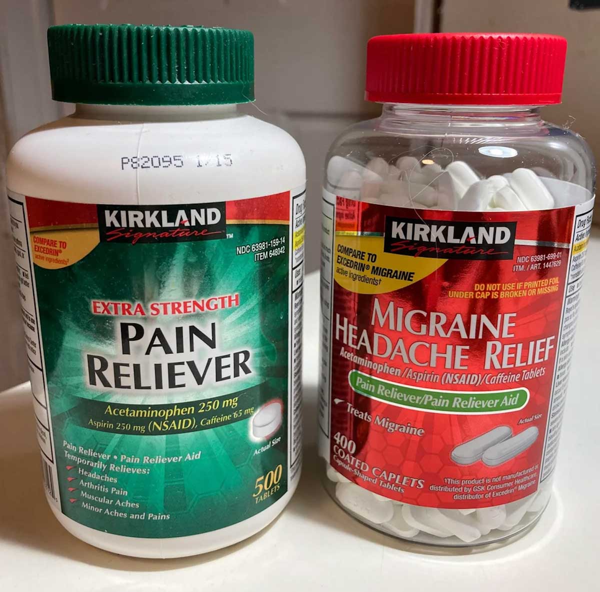 Two bottles of Kirkland Signature pain relief medication—often listed among Costco products to avoid—include "Extra Strength Pain Reliever" (acetaminophen) and "Migraine Headache Relief" (aspirin, acetaminophen, caffeine), both with visible white caplets.
